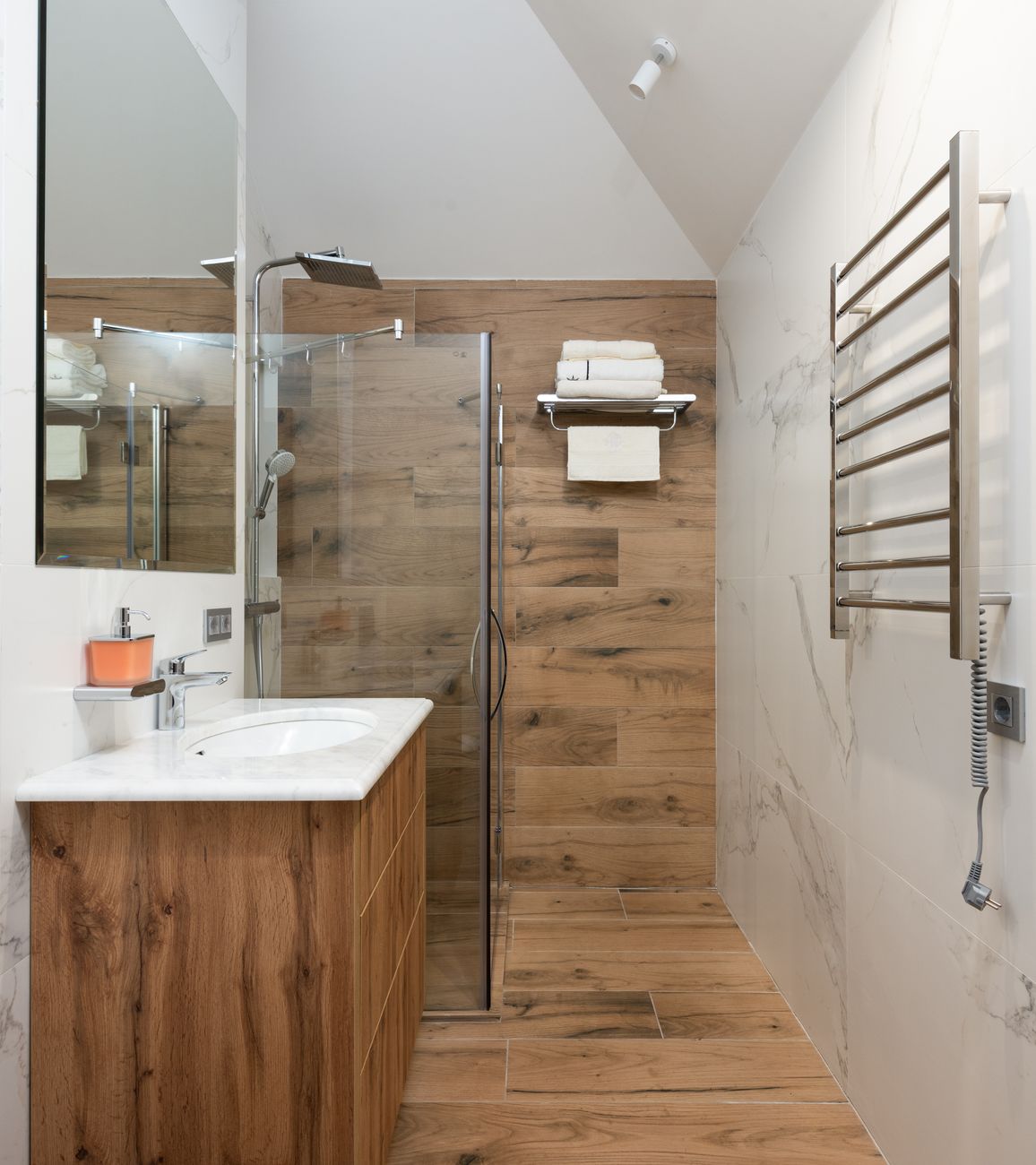 A newly finished bathroom in a real apartment with folded towels on a fitted rail, a mirror hung straight and a small plant on the sill — objects present, lived-in, the payoff of the hero's mid-tile wall